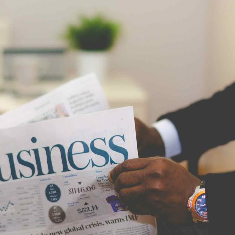 A person in a suit holding a newspaper with the headline Business and a report on a global crisis
