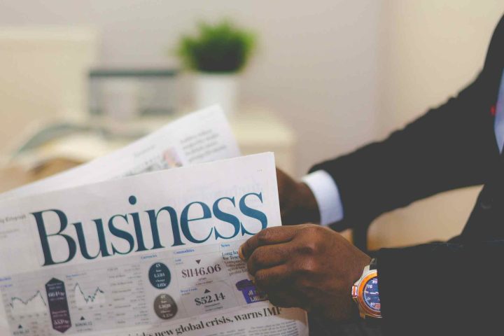 A person in a suit holding a newspaper with the headline Business and a report on a global crisis